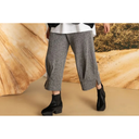 Wide-leg grey textured trousers with black ankle boots against earthy studio backdrop